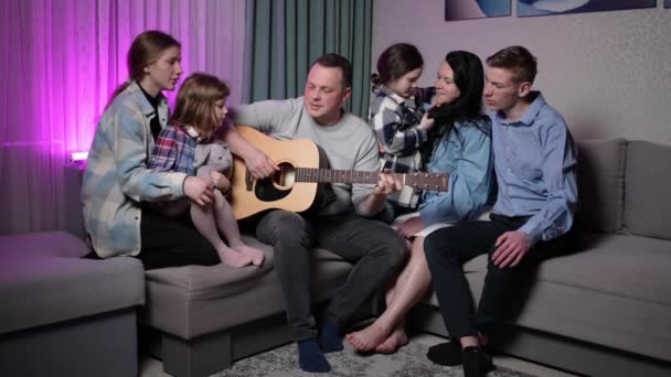 一个家庭在晚上回家休息的时候 一边对着吉他唱歌 一个慈爱的父亲弹奏吉他 全家人唱着歌 — 图库视频影像
