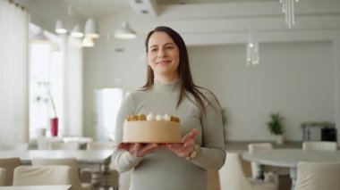 Tatmin olmuş gülümseyen bir kadın tatil için kremayla süslenmiş lezzetli bir pasta getirir ve bir restoranda masanın üzerine koyar.