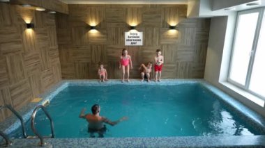 Çocuklar ilgili babalarıyla kapalı bir havuzda yüzerler.