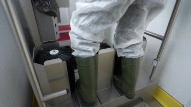 Koruyucu giysili biri ayakkabıları fırça ve dezenfektanla temizler.