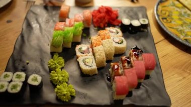 Japon yemek kompozisyonu. Ahşap arka planda siyah tabağa çeşitli suşi çeşitleri yerleştirilmiş..