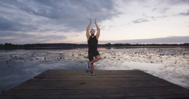 Bir adam mavi gökyüzünün batışında nehir kıyısında yoga yapıyor. Doğada pilates yapıyor. Sporcu profesyonel olarak egzersiz yapar.