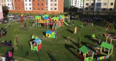 Ebeveynler çocuklarıyla birlikte bir sürü eğlencenin olduğu harika bir oyun bahçesinde yürürler.