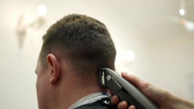 Elektrikli tıraş makinesiyle erkek saç kesimi. Kuaförde makineli saç stili. Kadın eli, bir erkeğin kafasındaki kılları elektrikli traş makinesiyle alıyor.