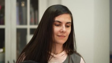 Hoş gülümseyen bir kuaför müşterinin saçını saç kurutma makinesiyle kurutuyor.