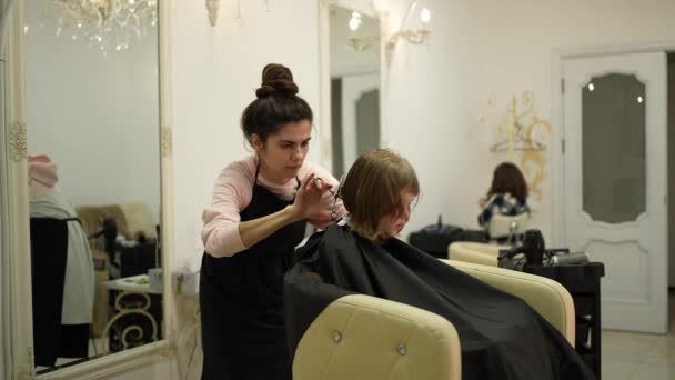 Kobieta Mistrz Obcina Włosy Małej Dziewczynki Siedzącej Krześle Fryzjerskim — Wideo stockowe