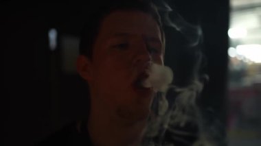Kafkasyalı genç adam buhar yapıyor. Genç adam nargile içiyor ve karanlık bir odada duman halkaları üflüyor..