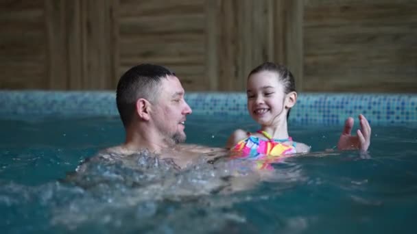 爸爸教他女儿在游泳池里游泳 儿童在水里的游戏和活动 一个父亲的爱和关心 水的安全 — 图库视频影像