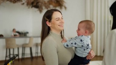 Sevecen, genç bir anne kucağında sevimli bir bebek, kucağında küçük bir bebekle öpüşüyor. Çocukluk kavramı, ebeveynlik. Güzel, mutlu bir aile.