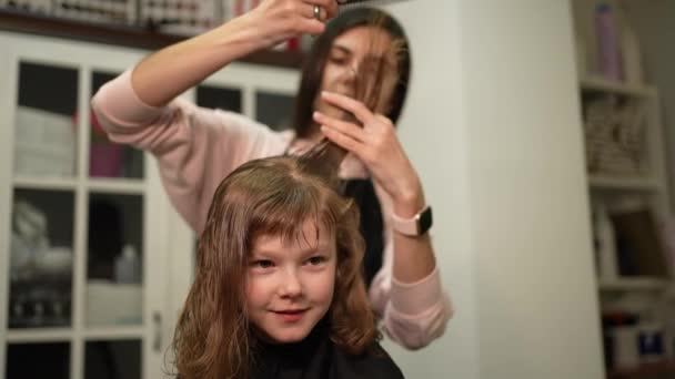 女性の美容師は少し陽気な女の子の髪の毛の端をトリム — ストック動画