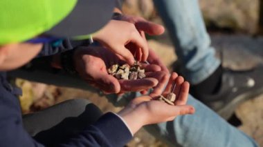 Tanınmayan bir baba oğluyla sahilde oturur, küçük taşlar toplarlar.