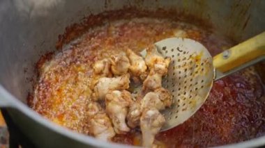 Tavuk açık havada büyük bir ızgara kazanda kızartılıyor, bir adam da mutfak kaşığıyla kızarmış yemekleri karıştırıyor. Sokak yemekleri, aşçılık konsepti.