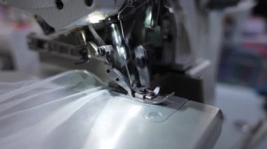 Dikiş makinesinin iğnesi hareket halinde. Dikiş makinesinin iğnesinin yakın çekimi hızla yukarı ve aşağı hareket ediyor. Bir terzi dikiş atölyesinde beyaz kumaş diker..