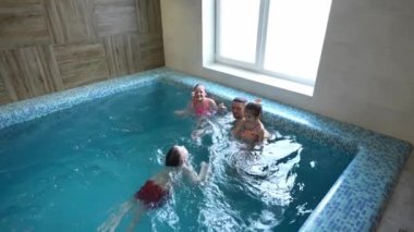 Bir baba ve üç çocuğu havuzda oynuyorlar. Bir baba kızını kollarına alır ve oğluna yüzmeyi öğretir..