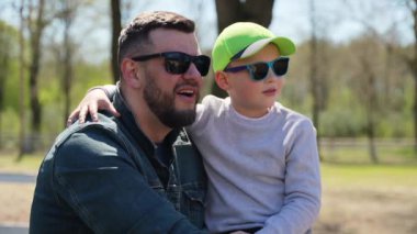 Bir çocuk dışarıda yürürken babasının yanında oturuyor ve gülümsüyor. Mutlu aile