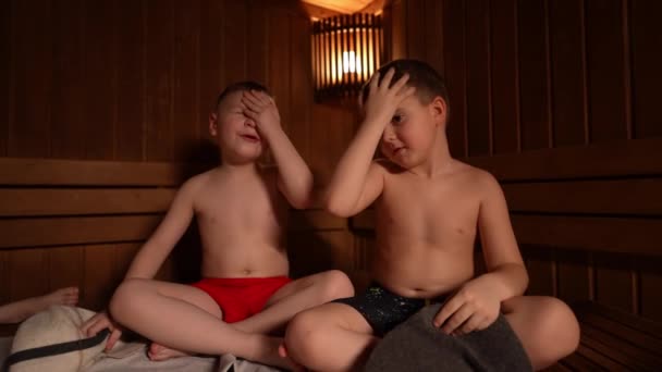 二人の小さな男の子が熱いサウナに座っています — ストック動画