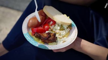 Bir kadın tek kullanımlık plastik çatallı kağıt kaseden kırmızı domates salatası ve ekmekle et yiyor.
