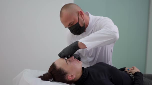 外科医生戴着医用手套和面具 按摩脸部 均匀地将透明质酸分布在眼睛下面 注射美容品整形手术 — 图库视频影像