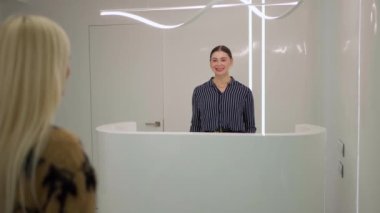 Gülümseyen genç ve çekici bir kız bir müşteriyle resepsiyonda buluşuyor.