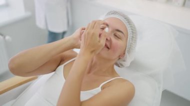 Kadınlar için kozmetik prosedürleri. Kozmetik bilimi için hazırlık. Kozmetik ameliyata başlamadan önce kadının kafasına tek kullanımlık bir başlık takıp saçlarını sakladı.