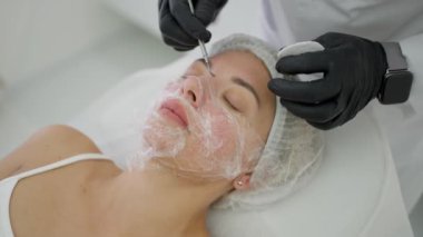 Profesyonel bir kozmetikçi güzellik salonunda bir hastanın yüzünü mekanik olarak temizler. Cilt bakımı. Yüz temizleme