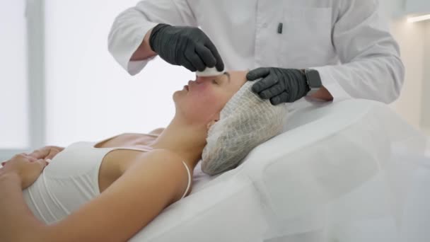皮膚科医は 化粧品の手順を行うために消毒化合物を患者の顔を拭く — ストック動画