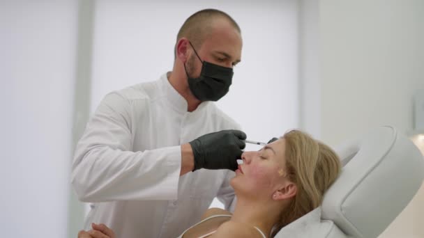 額の領域で若い女性のクライアントの顔に注射を行い美容師 — ストック動画