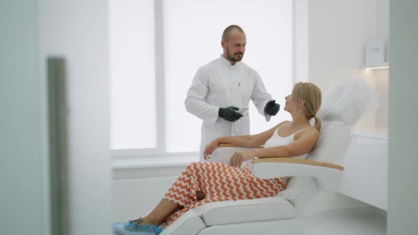 Uma Mulher Senta Uma Cadeira Cosmetologia Médico Sorri Fica Lado — Vídeo de Stock