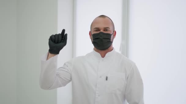 黒の保護マスクの医者は警告ジェスチャーを示す指を上げる — ストック動画