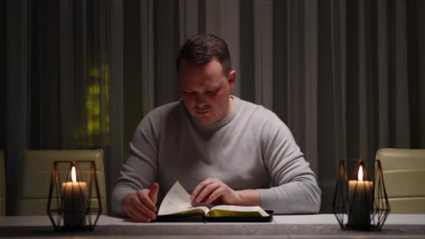 Мужчина Читает Книгу Свечах Сидя Столом Дома — стоковое видео