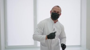 Tıp eldivenleri ve maskeli komik genç doktor iş yerinin yanında dans ederken eğleniyor.