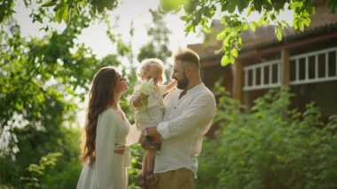 Mutlu bir aile, güneşli bir yaz gününde banliyö evinin arka bahçesinde dinlenirken oğluyla oynuyor.