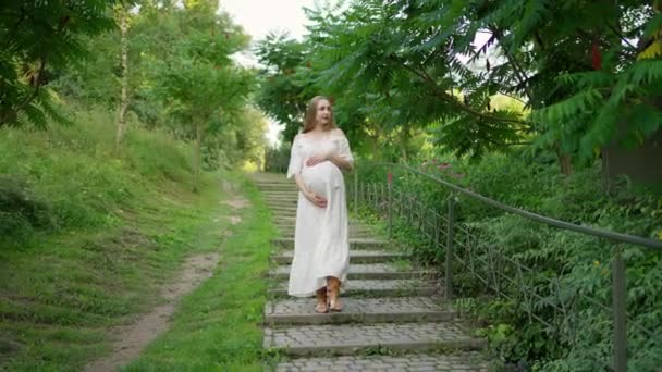 Μια Έγκυος Νεαρή Γυναίκα Περπατάει Στις Σκάλες Ένα Καταπράσινο Πάρκο — Αρχείο Βίντεο