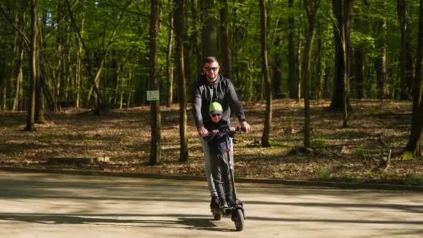 快乐的大胡子男人和他的小儿子一起骑电动车在城市公园里 — 图库视频影像