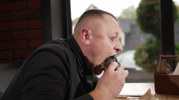 カフェに座っている男が野菜と肉でハンバーガーを食べる — ストック動画