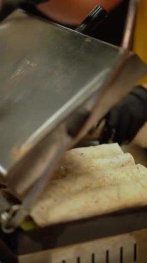 Lokantada siyah eldivenli profesyonel bir şef elektrikli ızgaraya pide koyar, kapağı kapatır ve onları pişirir..