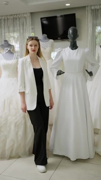 在婚纱店里 一个自信的女售货员站在穿着白色长裙的模特旁边 — 图库视频影像