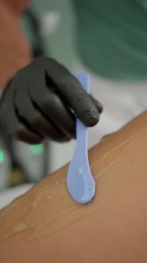 Tedavi odasında nazik bir ağda. Usta bir spatulayla müşterinin bacağına balmumu sürer.