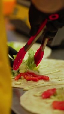 Sebze ve otlarla birlikte pide ekmeğinde kebap hazırlama süreci. Aşçı sebze ve domatesli doğranmış lahana ve soğan dilimlerini mutfak maşasıyla yayılmış pita ekmeğine serer..
