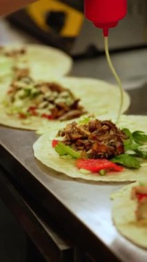 Şef fast food restoranında yemek pişirirken donör kebap ve shawarma 'ya beyaz sos döküyor. Pita ekmeğinin üzerinde sebze ve kızarmış etten bir sürü malzeme var. Yemek teslimatı