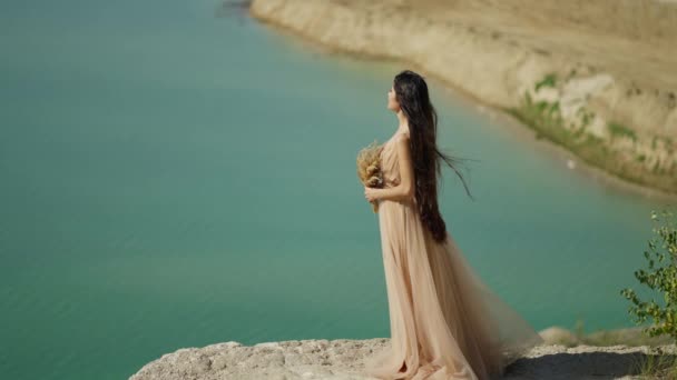 ウェディングドレスの若い花嫁が海の背景に岩の上に立っている — ストック動画