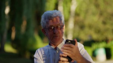 Mutlu yaşlı adam elinde akıllı bir telefonla cep telefonu ekranına bakarak selfie çekiyor.