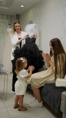 Bir anne ve küçük kızı, bir danışmanın seçenekler sunduğu bir mağazadan elbise seçerler.