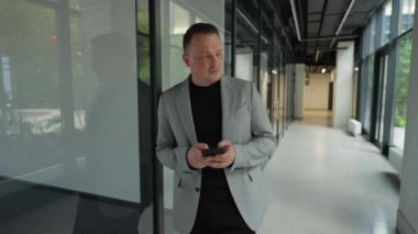 Adam üzgün, hayal kırıklığına uğramış, üzgün, kızgın, ofis merkezinde duruyor, canı sıkkın, telefona bakıyor ve aramasını bekliyor.