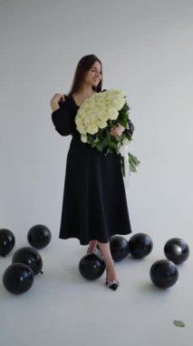 Stüdyoda beyaz arka planda bir buket gülle poz veren mutlu genç bir kadın.