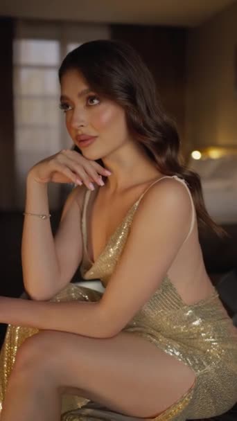 漂亮迷人的女人坐在沙发上打情骂俏 摆姿势看着镜头 穿着闪亮的衣服 时装广告概念 — 图库视频影像