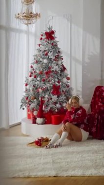 Seksi sarışın kız kruvasanla kahve içer ve yeni yıl sabahı kameraya gülümseyerek eğlenir.