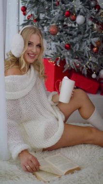 Evde kahve içen neşeli genç bir kadının portresi. Gülümseyen güzel kız sıcak çay içer. Genç sarışın kadın kış tatilinde sabah kahvesinin tadını çıkarıyor.