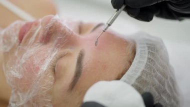 Eldivenli bir kozmetik uzmanı kozmetoloji kliniğinde genç bir kadının yüzünü temizler ve cilalar. Modern insanlar için profesyonel donanım nemlendirme ve gençleştirme prosedürleri.