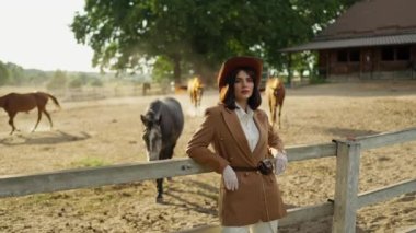 Siyah saçlı çekici bir kadın binici ayakta, dinleniyor ve yakınlarda bir at otluyor. Atlı bir kadın çiftlikte vakit geçirir, aygıra koşar, yemek yemesini bekler.
